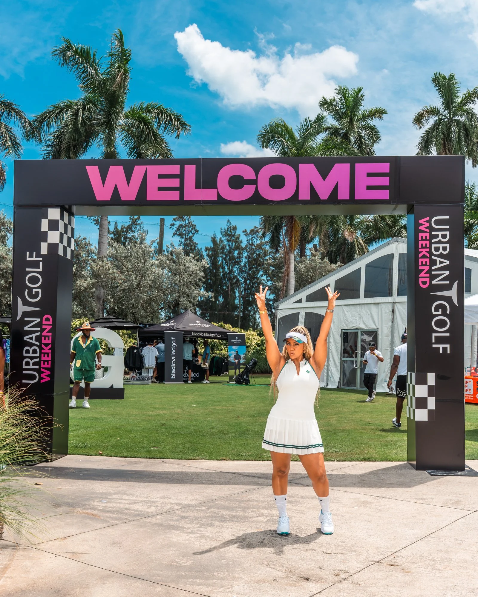 Woman celebrating under the Urban Golf Weekend welcome arch in Miami
